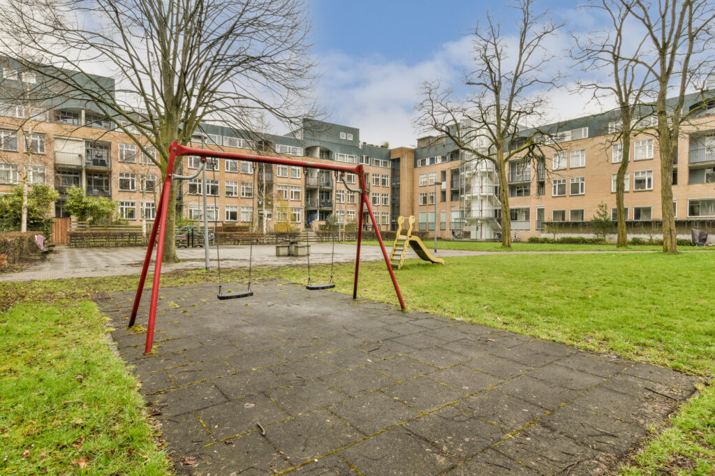 a communal garden for residential flats with a playground and lawn surrounded by trees